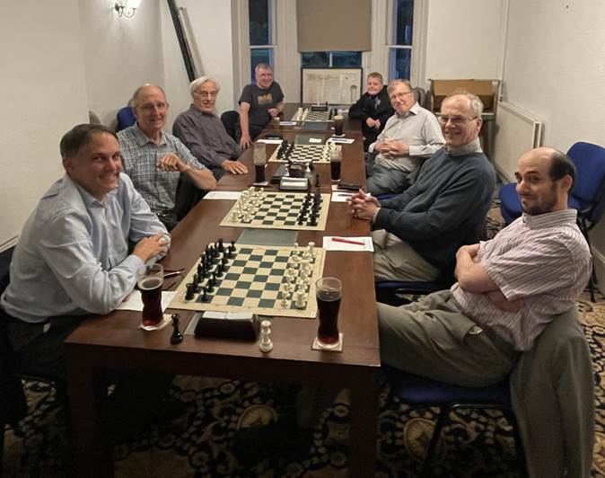 A group of men sitting around a table with chess board

Description automatically generated